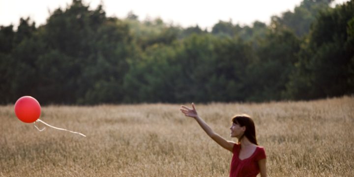 Girl standing in field letting go of a red balloon.